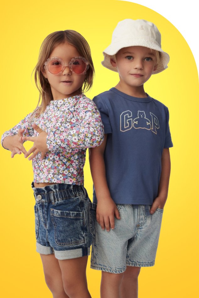 Duas crianças usando óculos de sol e chapéus, posando lado a lado com sorrisos alegres em um dia ensolarado.
