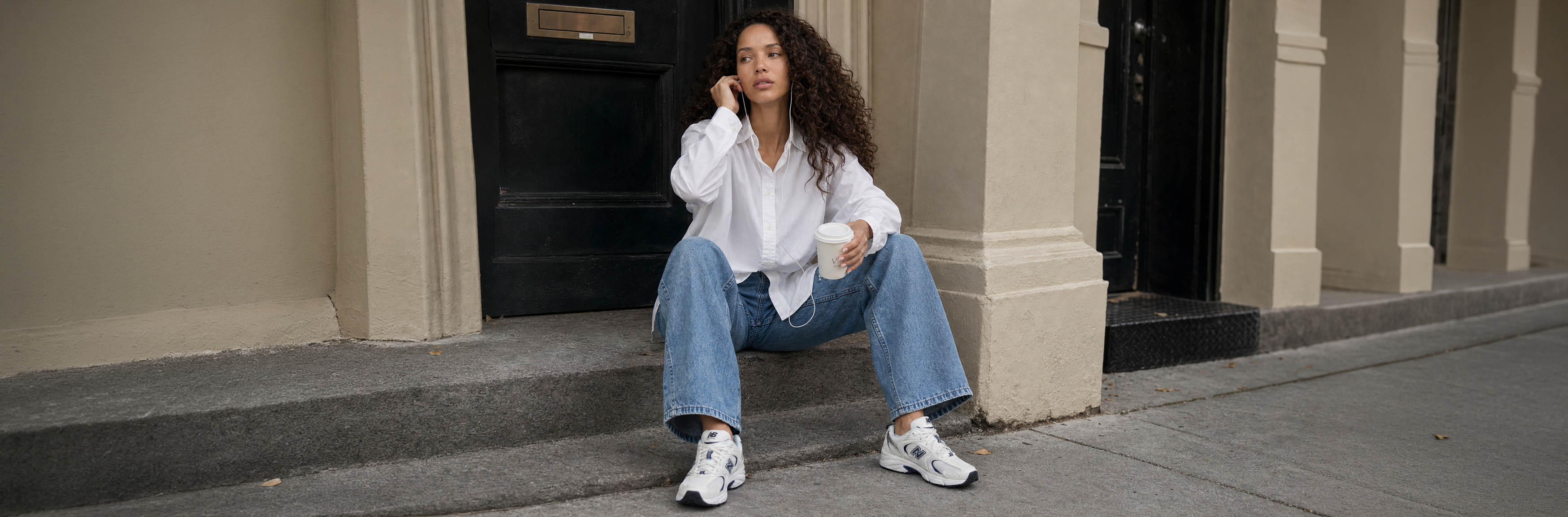 Mulher vestindo camisa branca, calça jeans e tênis New Balance branco.