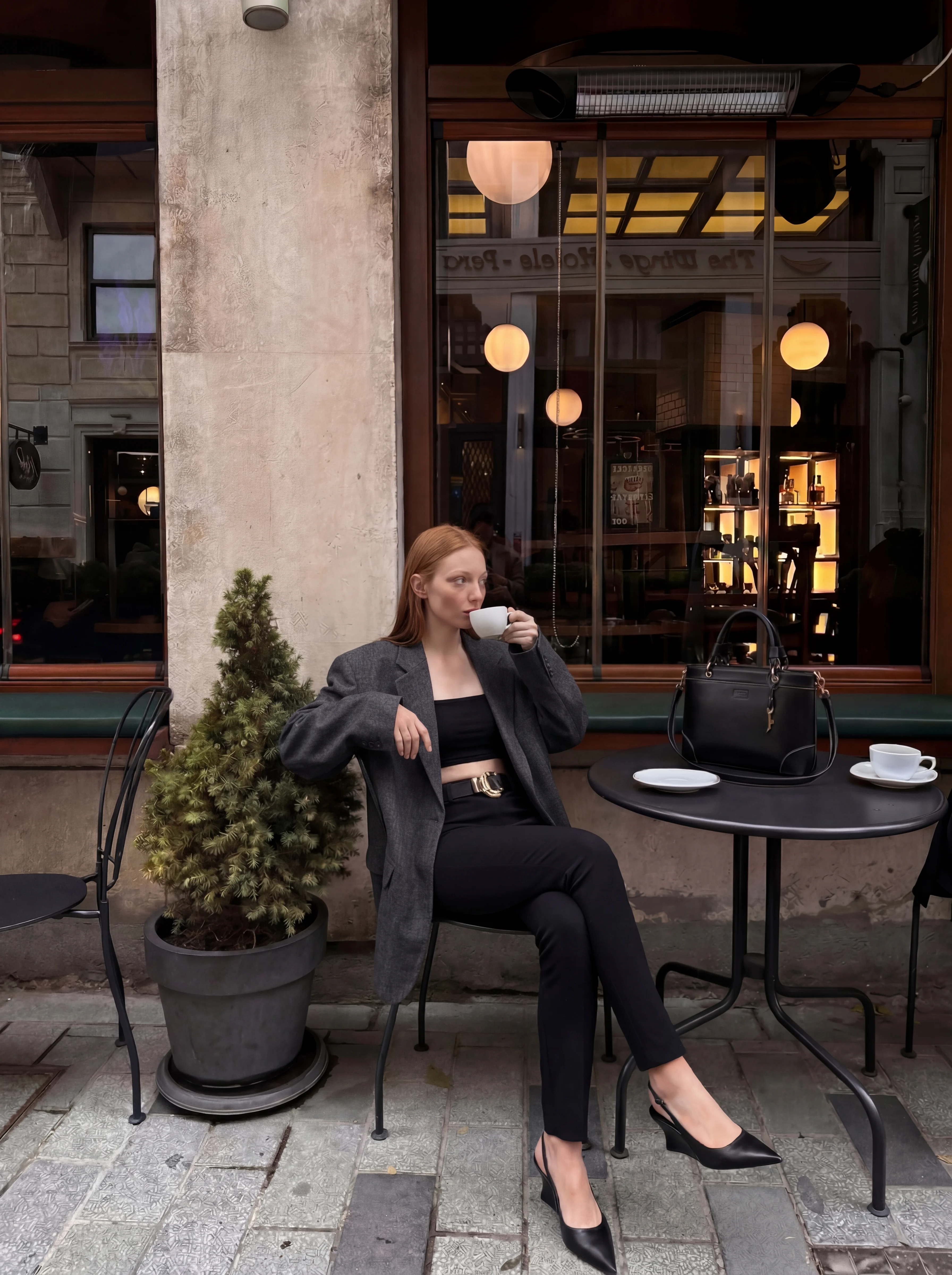 Mulher tomando café vestindo blazer e calça jeans.