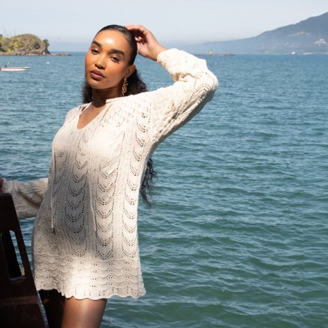 Mulher vestindo roupa de linho à beira do mar, transmitindo tranquilidade e harmonia com a natureza ao seu redor.