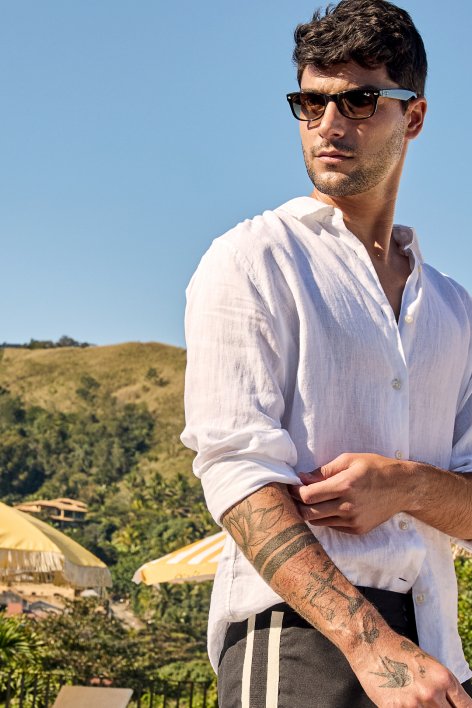 Um homem com várias tatuagens, usando uma camisa branca, que realça sua aparência única e estilizada.