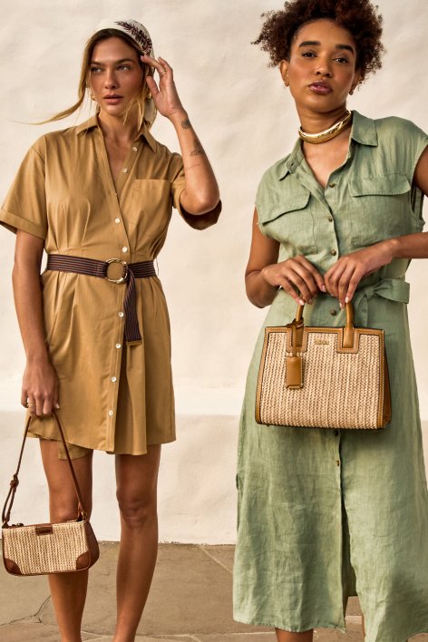 Duas mulheres, uma de vestido bege e outra de vestido verde, com bolsas marrons, posando em um local ao ar livre.