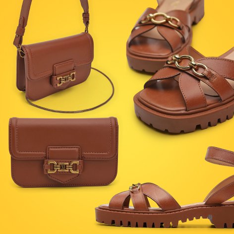 Sandália de couro marrom, bolsa e sapatos dispostos em uma superfície clara, destacando a elegância dos acessórios.