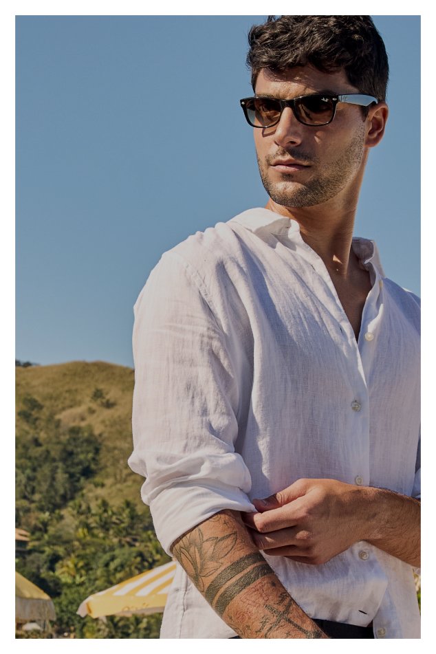 Um homem com várias tatuagens, usando uma camisa branca, que realça sua aparência única e estilizada.