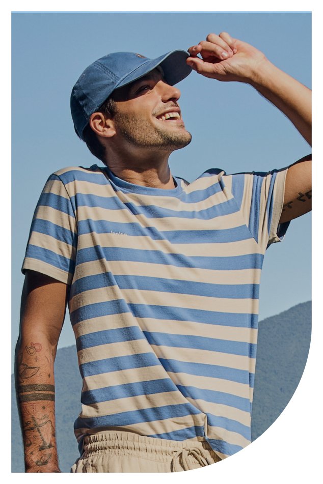 Homem usando uma camisa listrada azul e branca, acompanhado de um chapéu, em um ambiente ao ar livre.
