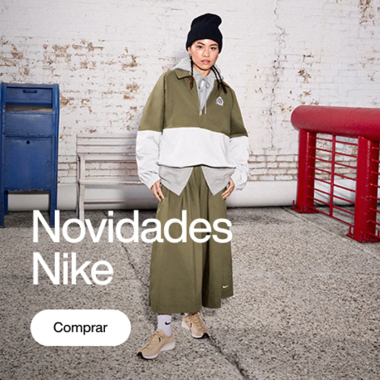 Modelo usando conjunto Nike verde-oliva e branco, gorro preto e tênis claros, posando diante de parede de tijolos brancos, caixa azul e corrimão vermelho. Texto: “Novidades Nike” e botão “Comprar”.